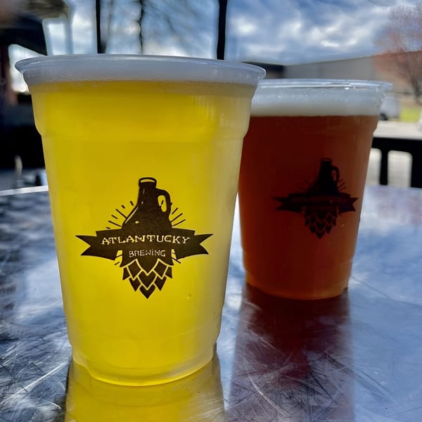 Two Atlantucky Brewing beers, one light and one amber, on a metallic table outdoors.