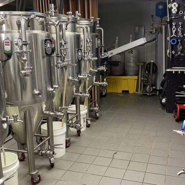 Stainless steel brewing tanks with gauges and pipes line a tiled floor at Atlantucky Brewing.