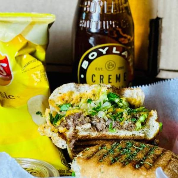 A grilled sandwich with meat and greens, a bag of chips, and a Boylan Creme soda.