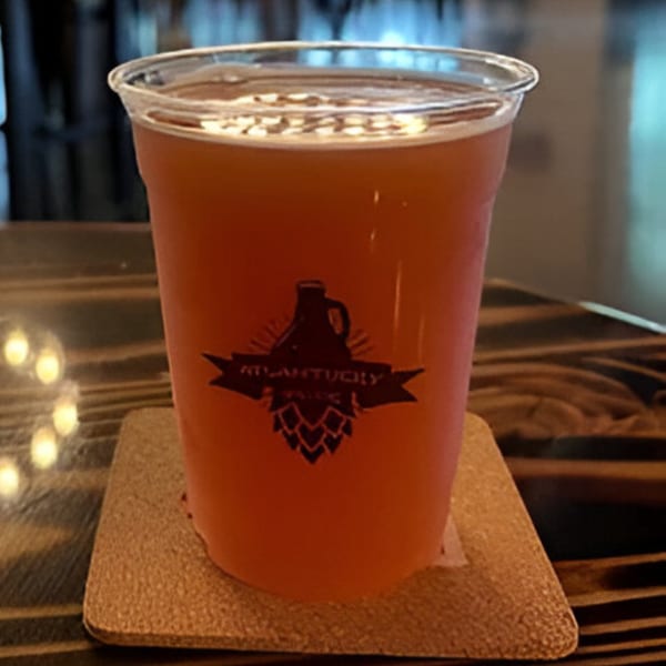 A plastic cup of Atlantucky Brewing beer with a logo on a coaster on a wooden table.