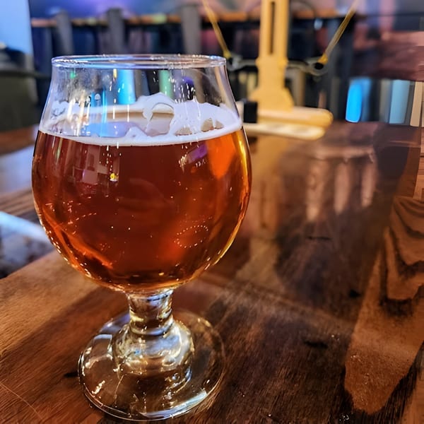 A glass of Atlantucky Brewing beer with foam on a wooden table, with blurred background.