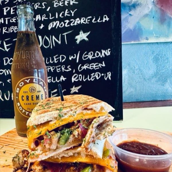 A Boylan Creme soda bottle next to a grilled sandwich with melted cheese and a side of sauce.