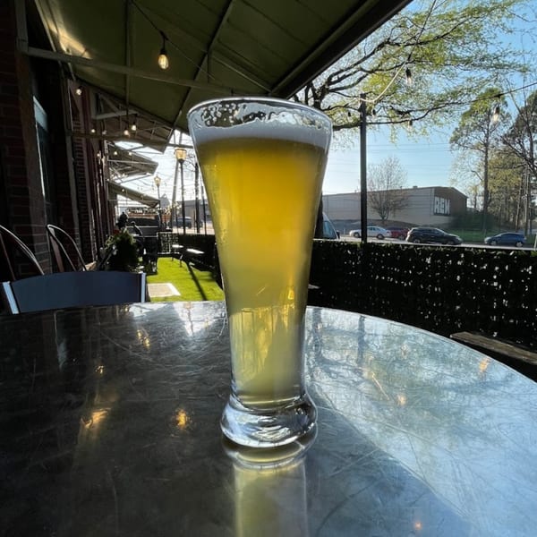 A tall glass of Atlantucky Brewing beer sits on a patio table with an outdoor view.