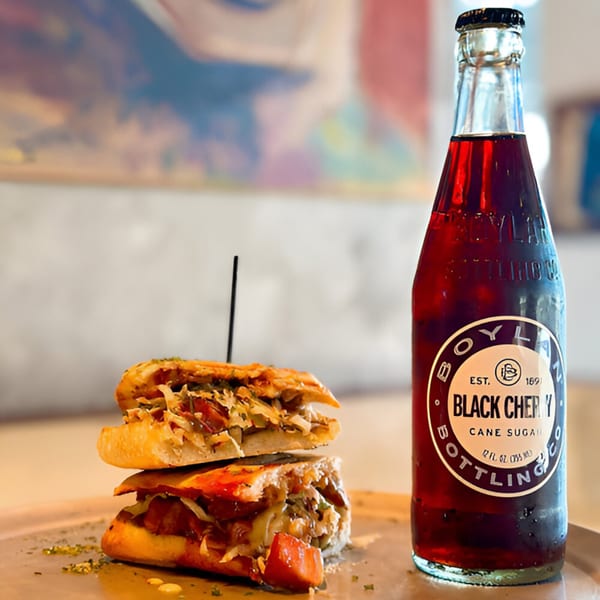 A Boylan Black Cherry soda bottle next to a hearty Atlantucky Brewing sandwich on a tray.