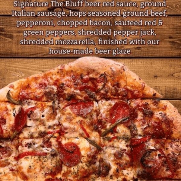 Close-up of a pizza with pepperoni, sausage, peppers, and cheese on a wooden surface.