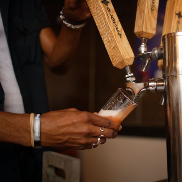 A bartender pours a frothy beer from a tap with a wooden handle into a glass at Atlantucky Brewing.