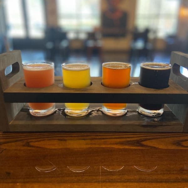 A wooden flight paddle holds four glasses of Atlantucky Brewing's craft beer, in various colors.